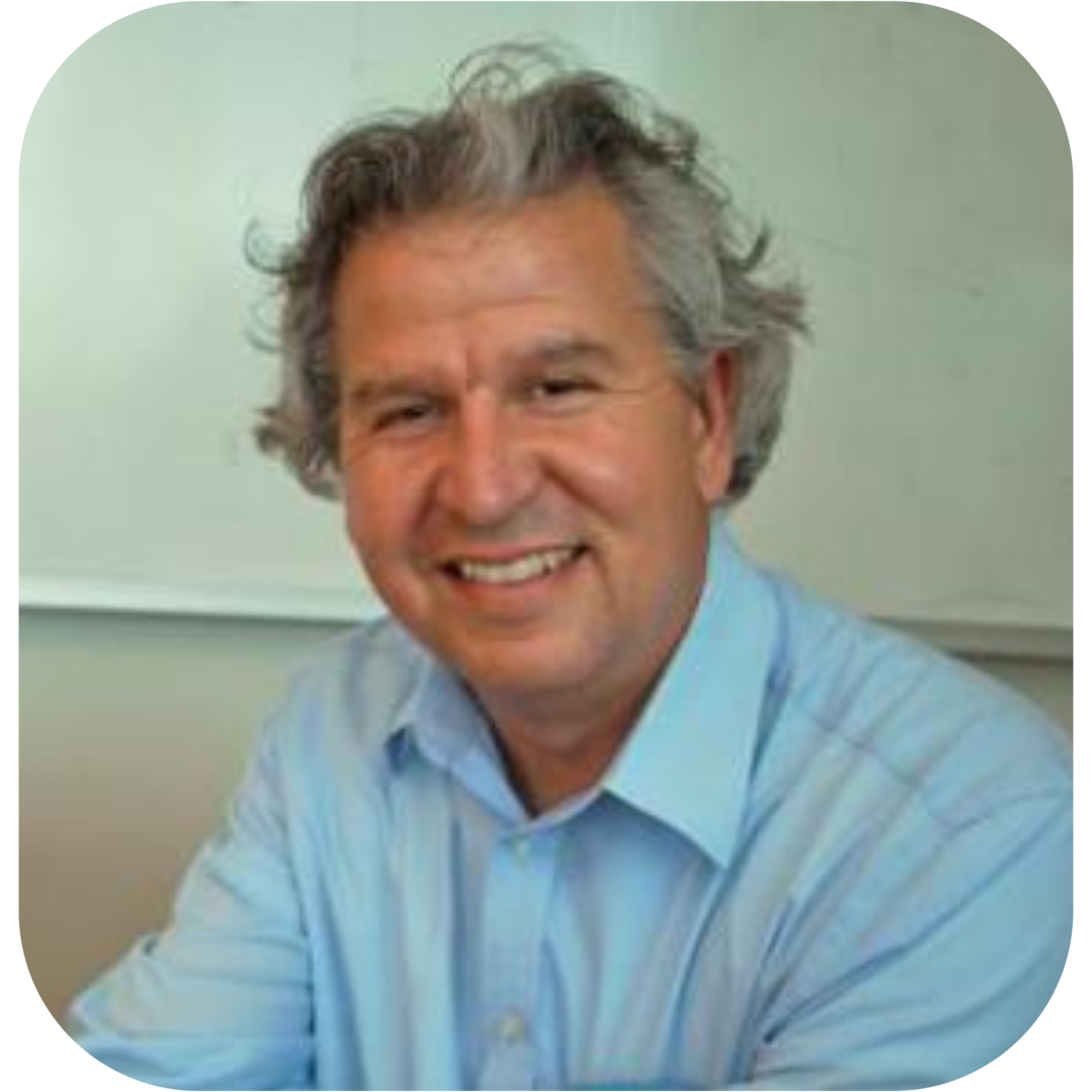 Rudy is a white male with fluffy graying hair and a charming smile. He's wearing a blue button down shirt and sitting in front of a white background.